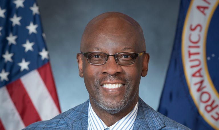 Portrait of Rickey Shyne, with U.S. and NASA flags in the background.