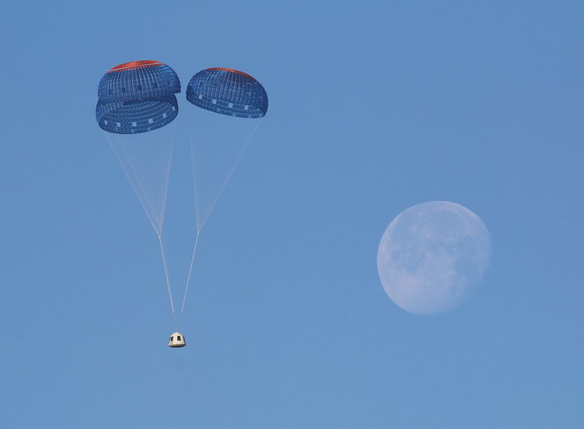 Blue Origin's New Shepard crew capsule under three parachutes in blue sky with Moon in background