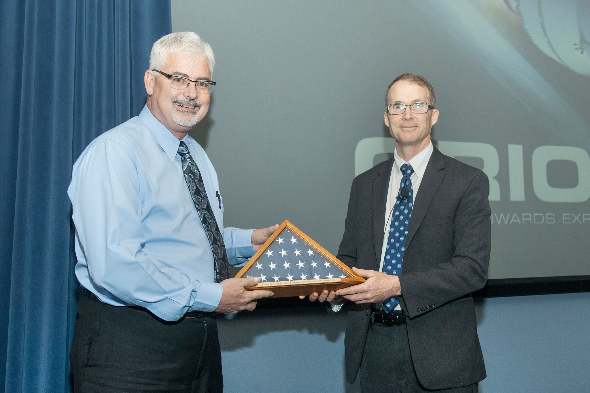 Charlie Lundquist, NASA Orion deputy program manager, right, presents an American flag flown aboard the Orion capsule.