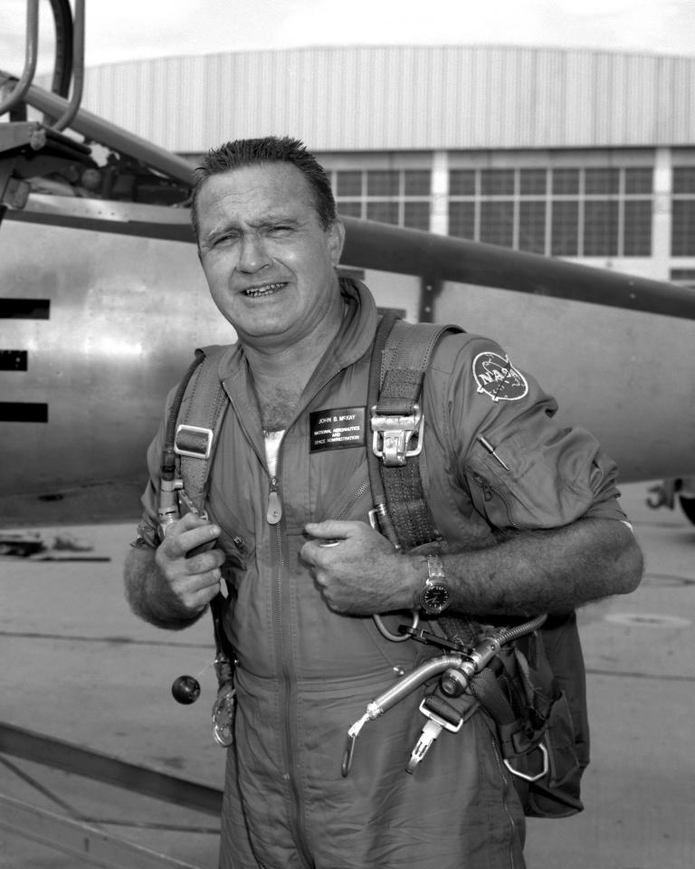 Black and white photo of a man in a flight suit in front of an aircraft.