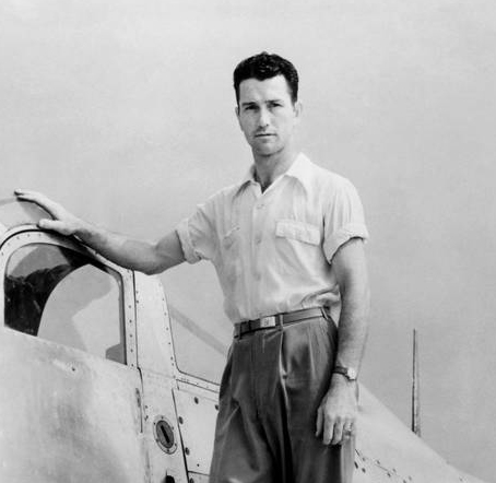 Black and white photo of a man posed on an aircraft.