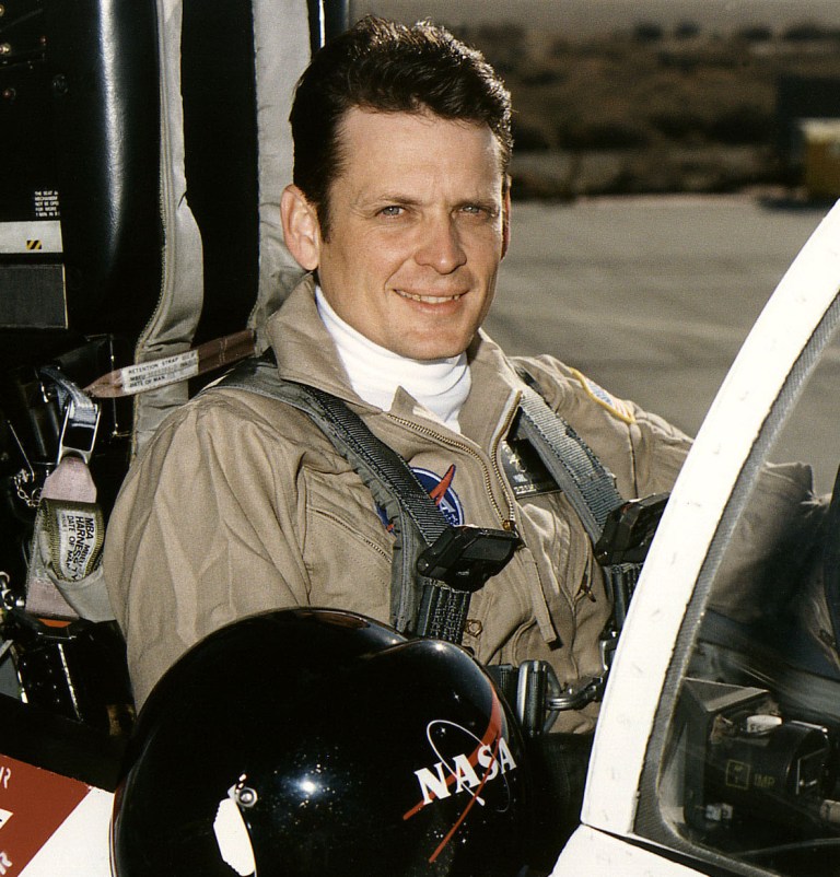 Man in flight suit sitting in cockpit.