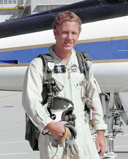 Man in flight suit, posed in front of aircraft.