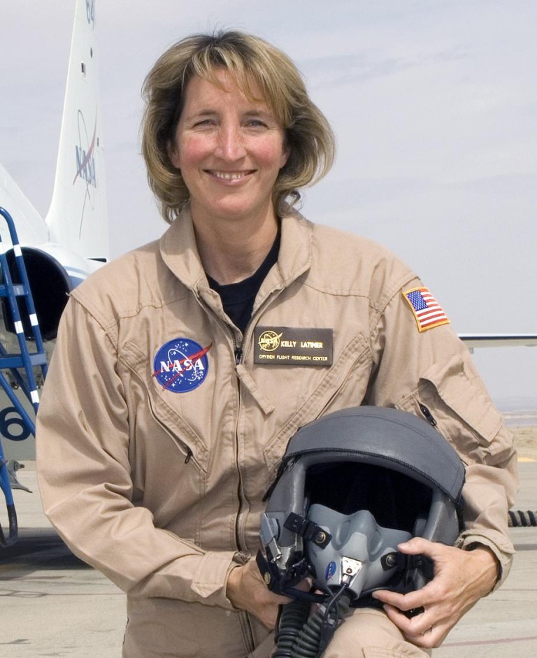 Woman in flight suit posed holding helmet.