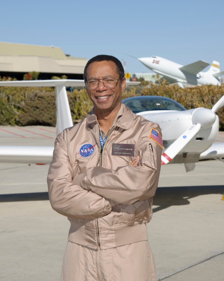 Man in flight suit posed in front of aircraft, smiling.