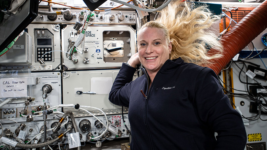 NASA astronaut and Expedition 64 Flight Engineer Kate Rubins poses for a photograph with a variety of space research gear and science racks behind her.