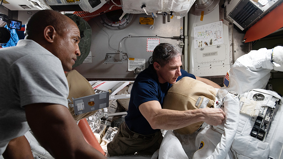 NASA astronauts Victor Glover (left) and Michael Hopkins work on U.S. spacesuit maintenance inside the International Space Station's Quest airlock.