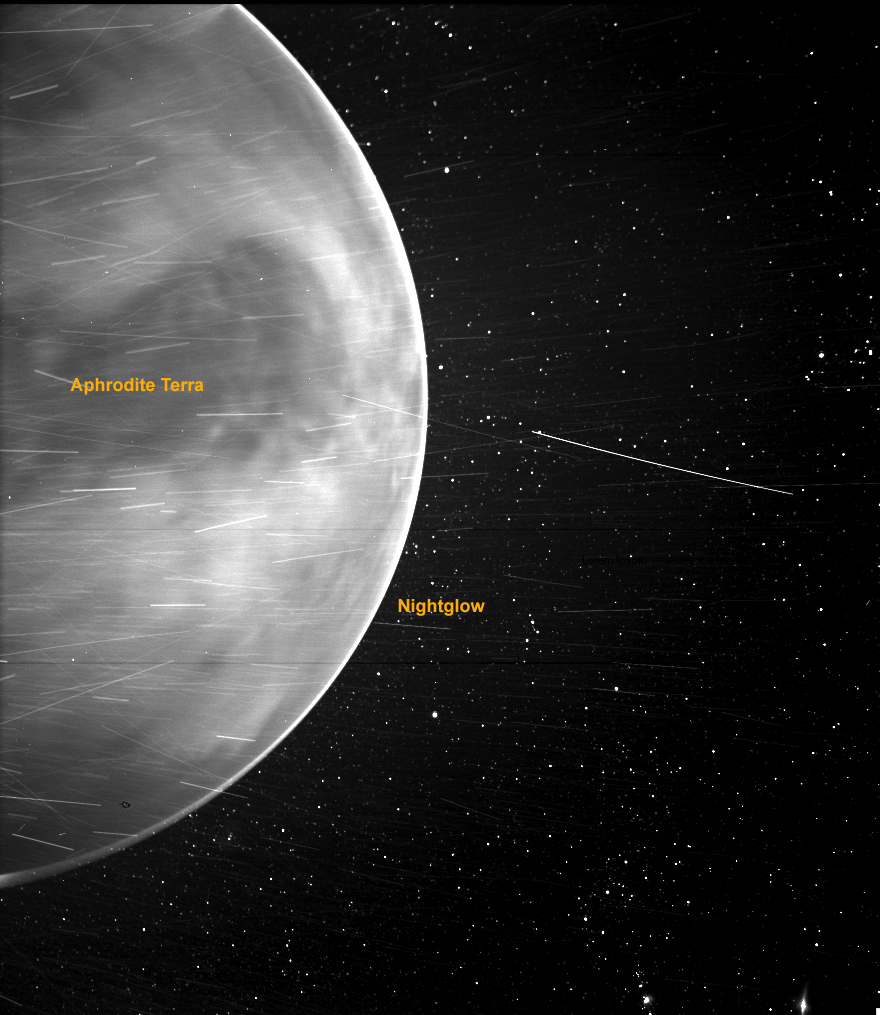 A black-and-white image shows one hemisphere of planet Venus against a backdrop of stars, with bright streaks throughout. The name Aphrodite Terra appears over a dark region on the planet, and the word Nightglow appears next to the edge of the planet, which appears brighter than the rest of the planet.