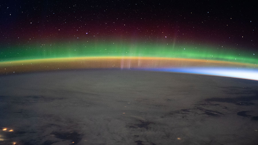 A bright aurora crowns Earth's horizon beneath a starry sky as the International Space Station flew into an orbital sunrise.