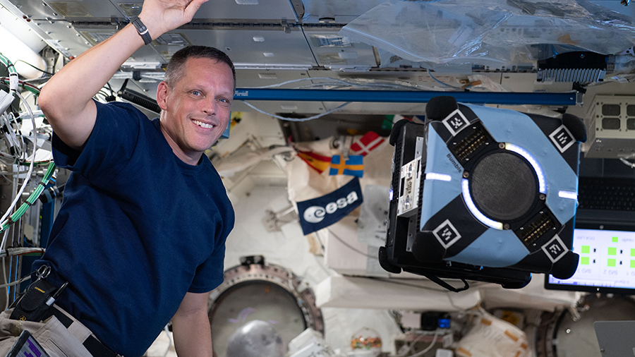 Astronaut Bob Hines monitors an Astrobee robotic free-flyer using smartphone technology to autonomously navigate and maneuver inside the station.