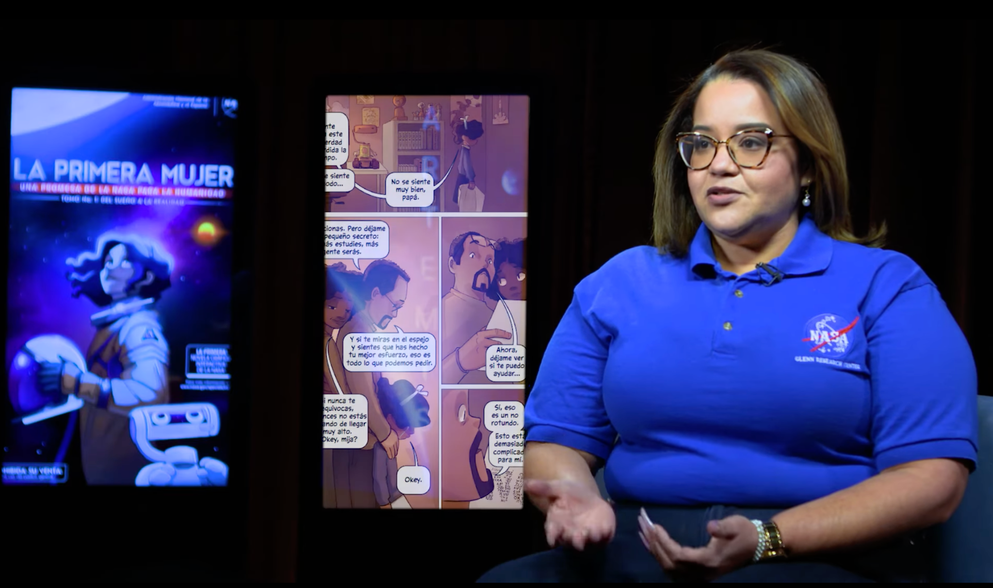 Dionne Hernandez-Lugo sitting next to screens displaying the Spanish language version of NASA's graphic novel, “First Woman."