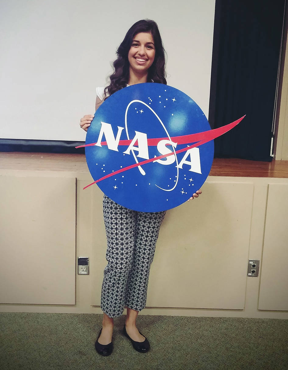 Intern holding a NASA Logo sign and smiling at the camera.