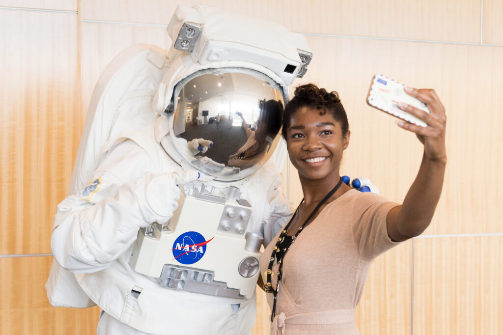 An intern taking a selfie with someone in an astronaut suit