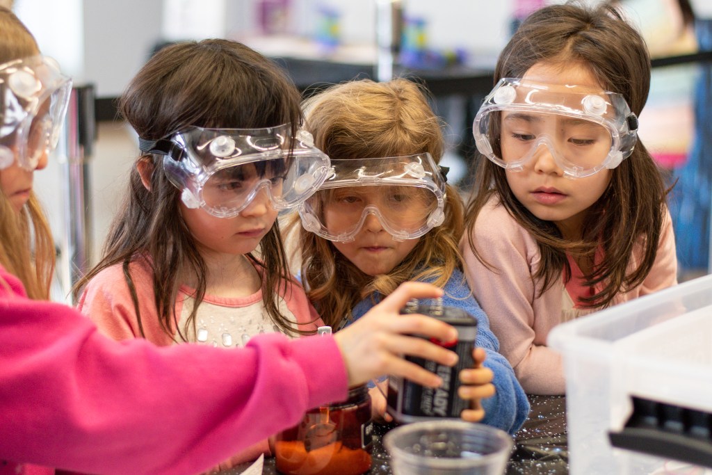 Four young students with safety glasses on working on an experiment, stem engagement