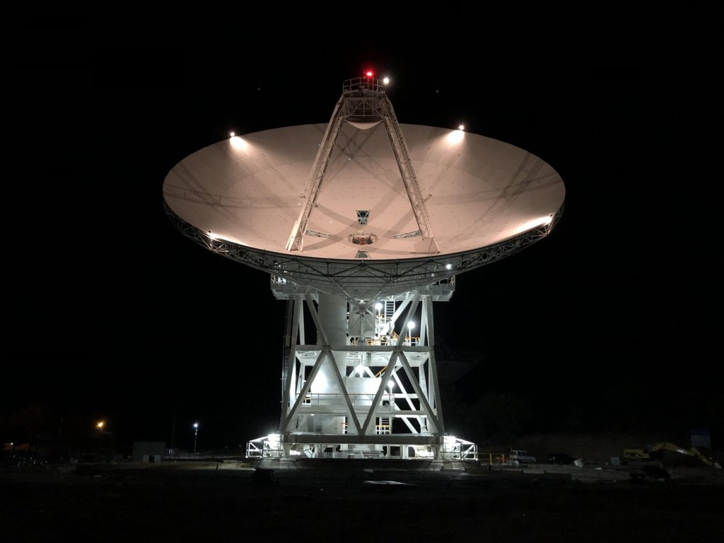 An antenna points to the sky, lighting up a dark black background.