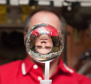 An astronaut looking at a reflection of himself in a droplet of water