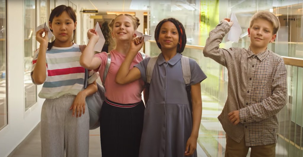 A group of four diverse children stand in a line and prepare to throw paper airplanes