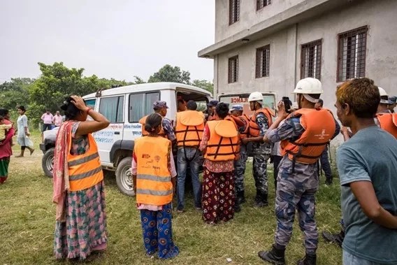 A group of people stand around a van in orange vests working on a flood simulation in Nepal.