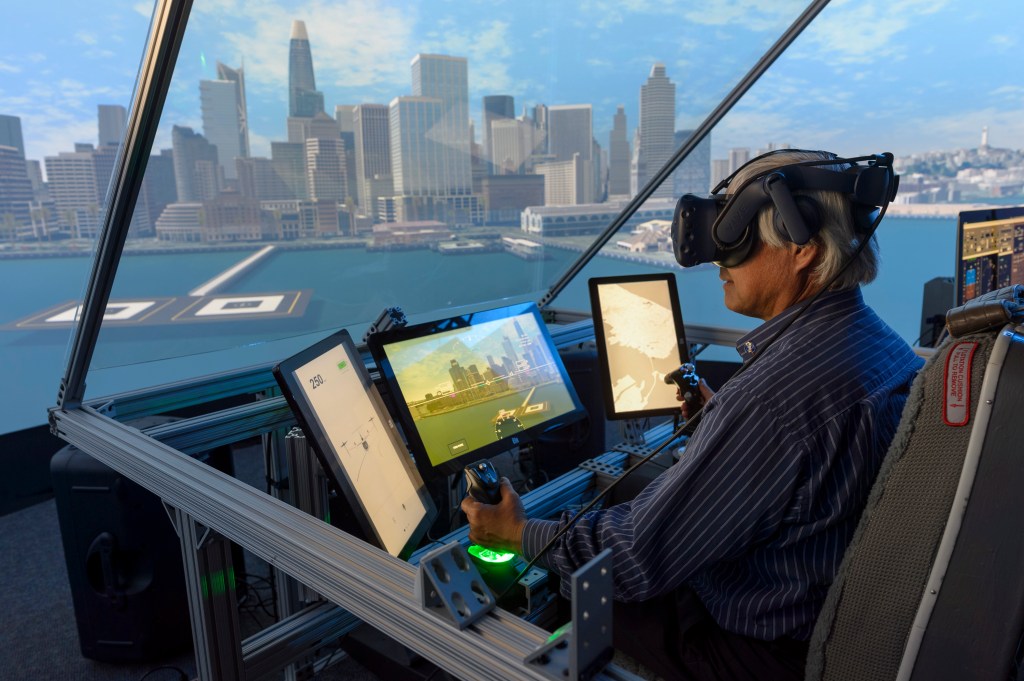 A technician wears a virtual reality headset and pilots an aircraft in a simulation.