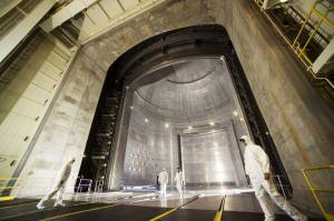 Four technicians walking in front of a large silver cylindrical chamber