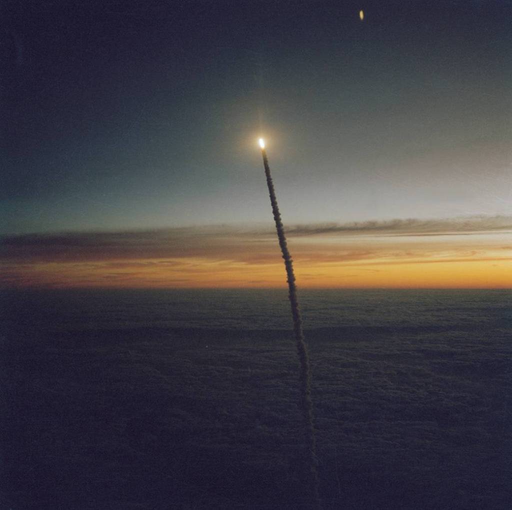 Shuttle Challenger flies above the clouds during a dawn launch, photographed from the air by a Shuttle training aircraft