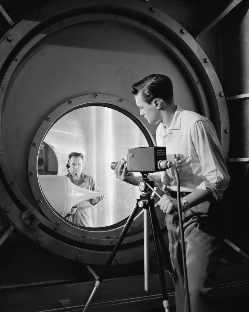 A television camera is focused by a NACA technician on a ramjet engine model through the schlieren optical windows of the 10- by