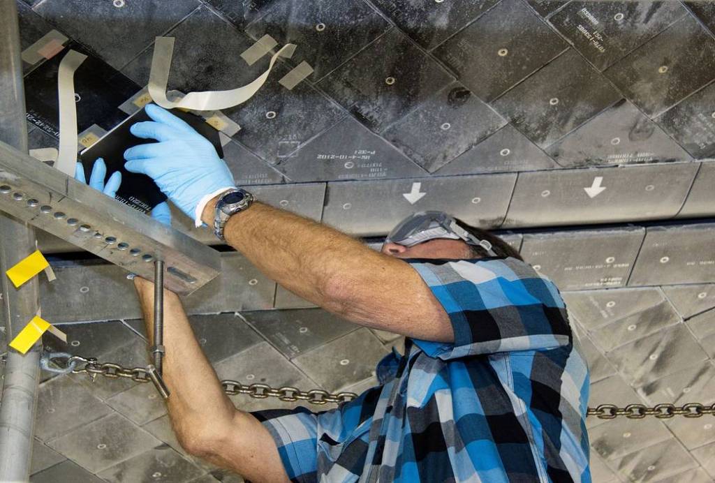 In Orbiter Processing Facility-1, a thermal protection system technician inspects the area on shuttle Atlantis' underside before a heat shield tile is installed. 