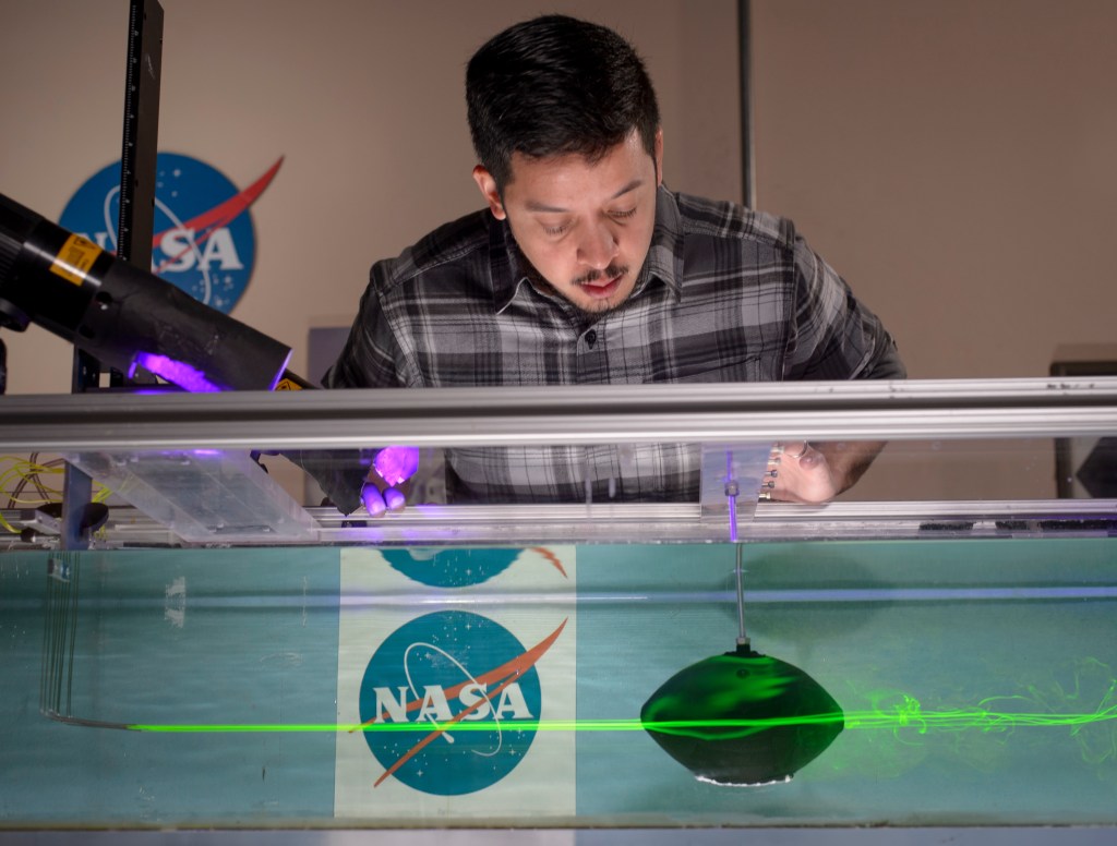 man looking at football in a water chamber with lasers and smoke around football