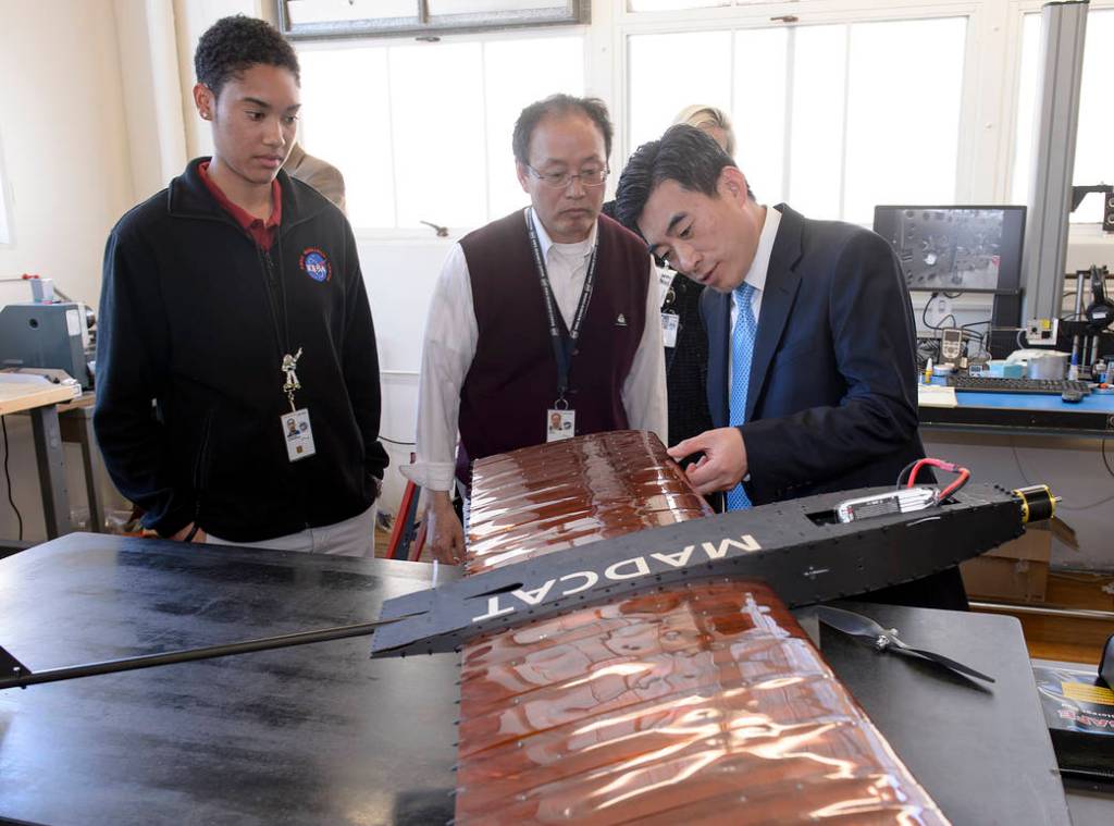 Three people looking at a small experimental aircraft on table.