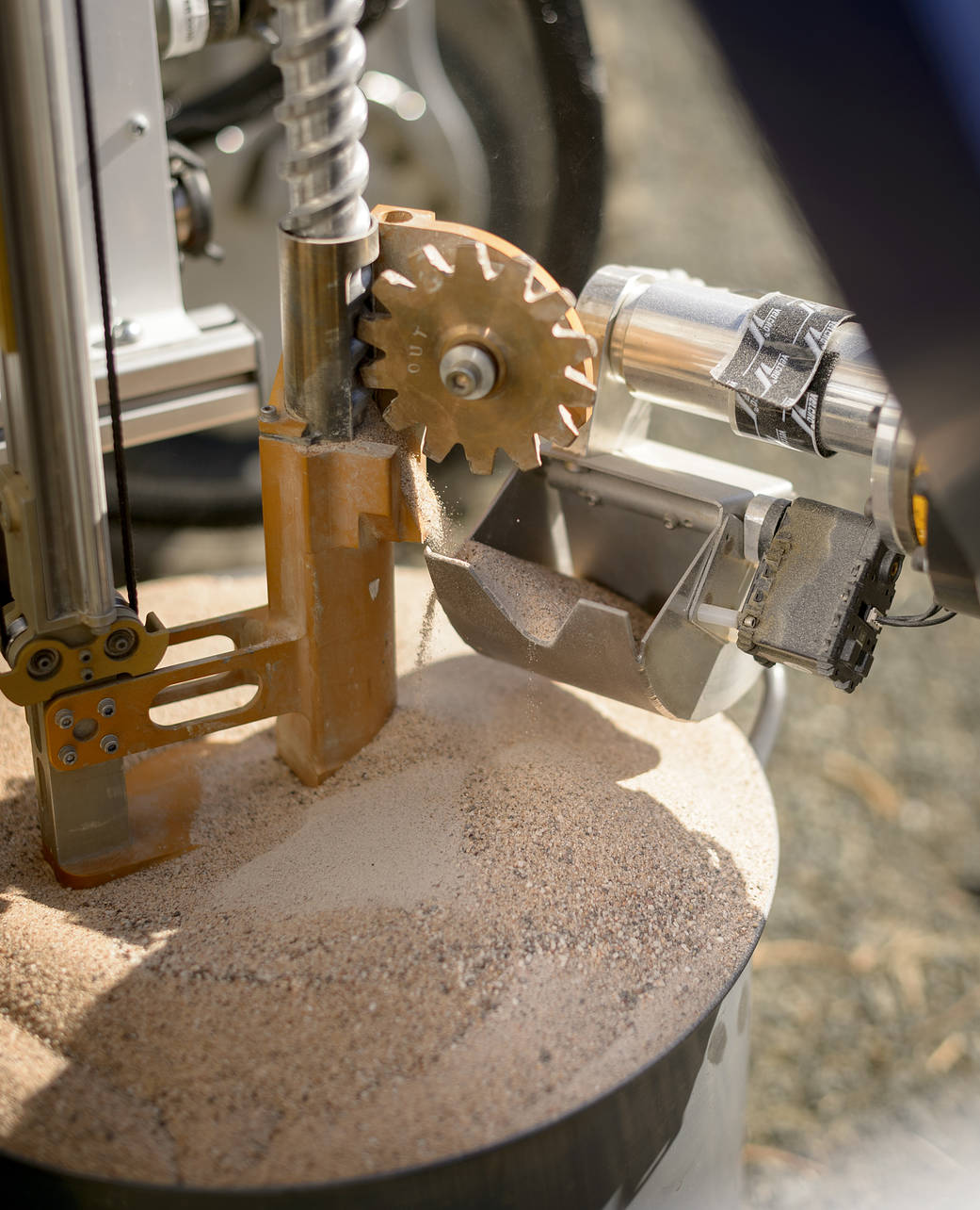 A sandy soil sample pours into the collection scoop, in this close-up of the ARADS life-detection rover.