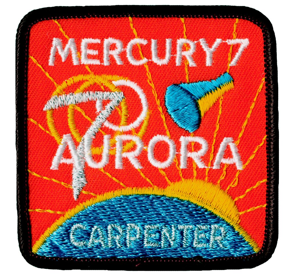 Mission patch for Mercury Atlas 7: Aurora 7 showing a Mercury capsule above the Earth with the sun peeking out behind the planet. Carpenter appears at the bottom of the patch.