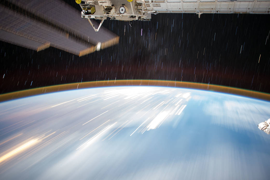 Earth and starry sky photographed from low Earth orbit with space station module at top of frame