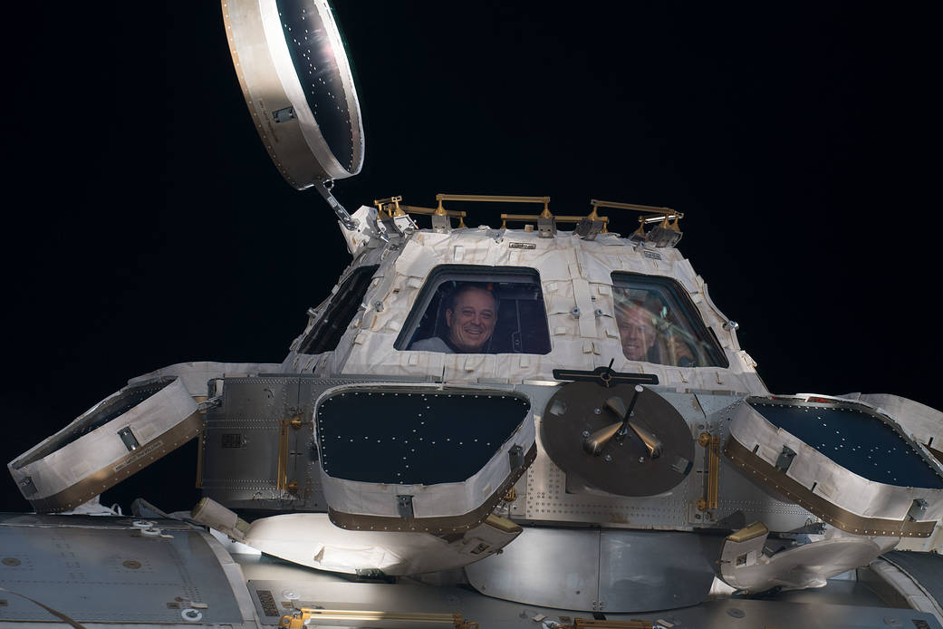 Astronauts Ricky Arnold and Drew Feustel peer out from inside the Cupola