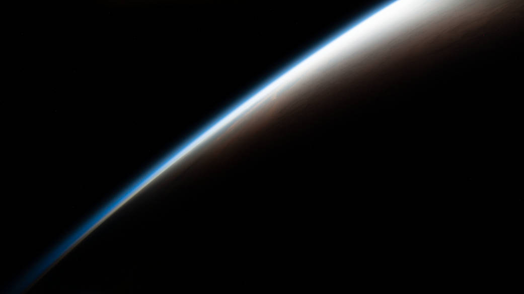 An orbital sunrise begins illuminating Earth's atmosphere