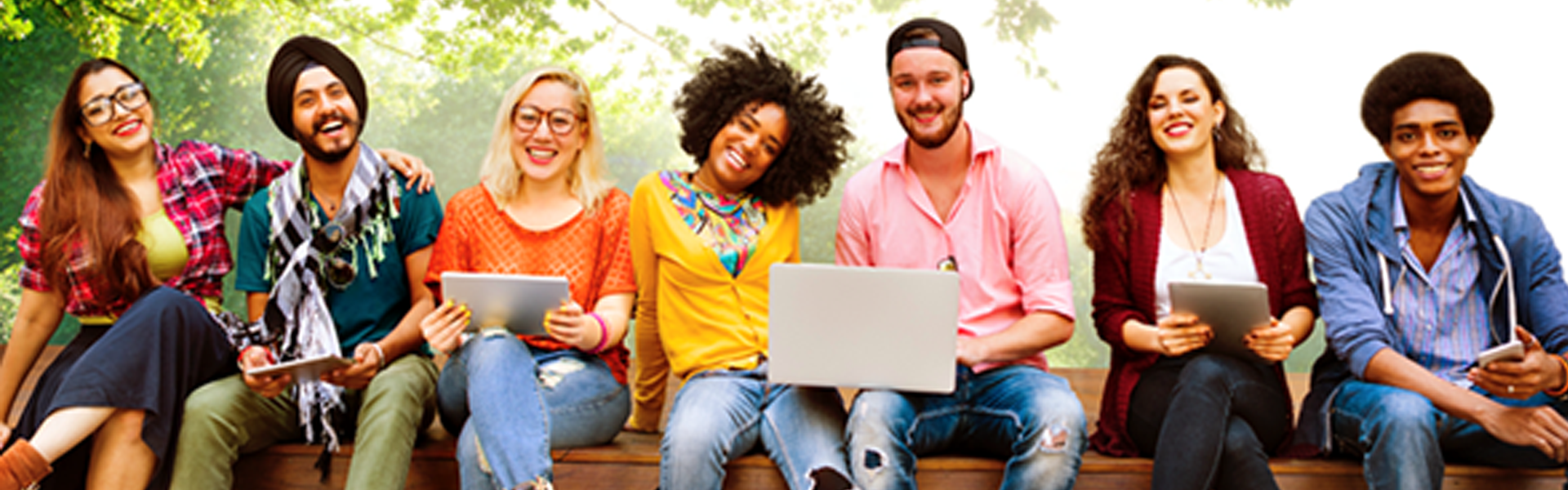 Group of college students sitting outside on a ledge with laptops and ipads