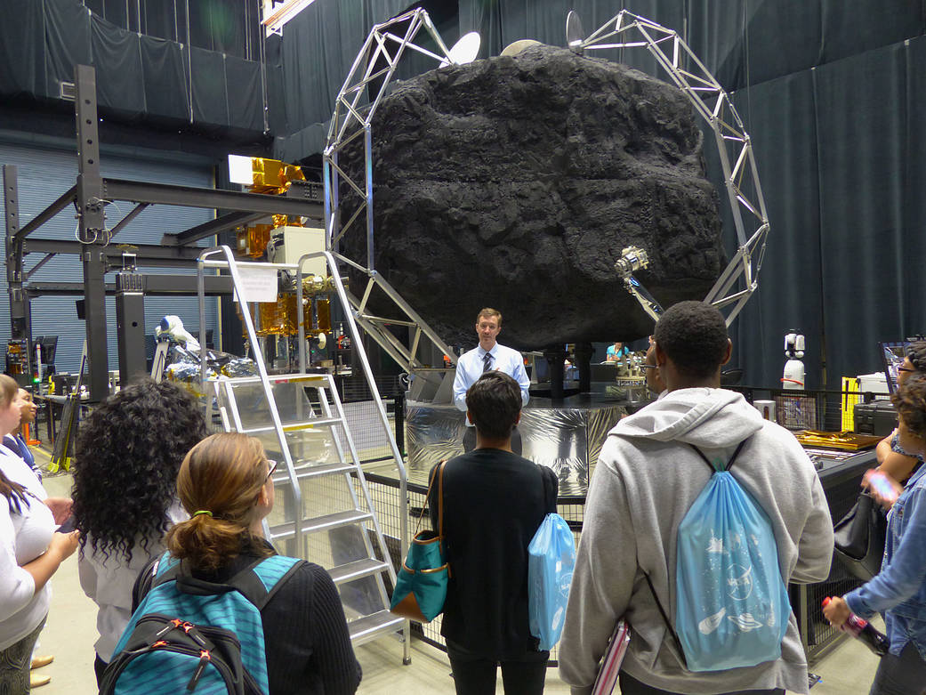 people surround a large simulated rock in a scaffold