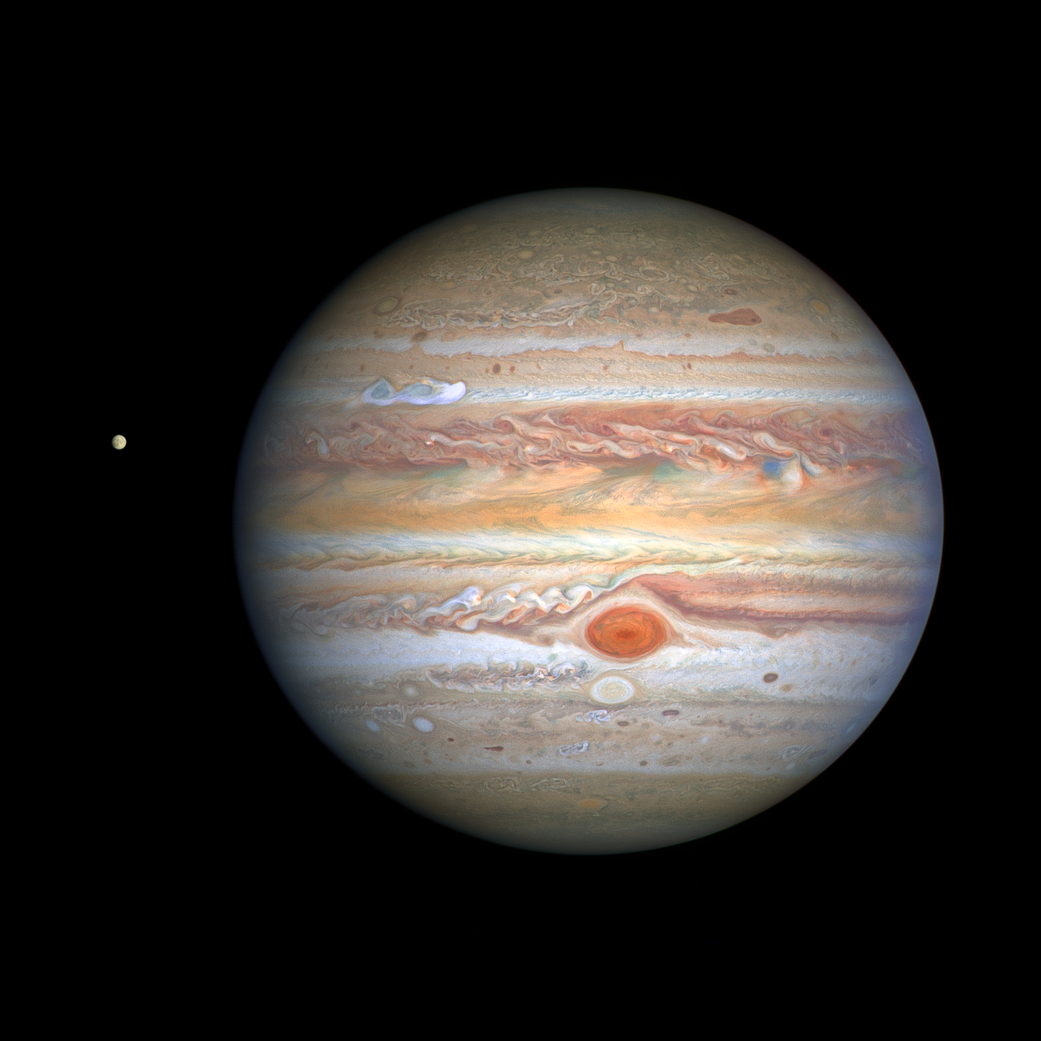 banded Jupiter with Great Red Spot and comparatively tiny moon Europa at left