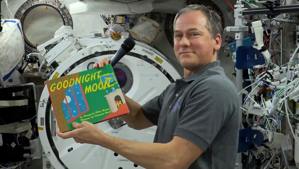 An astronaut holding a storybook inside the ISS