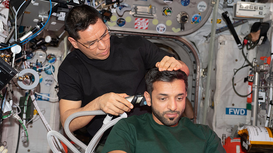 Astronaut Sultan Alneyadi receives a haircut from astronaut Frank Rubio aboard the space station with a hair trimmer containing a suction device collecting loose hair.