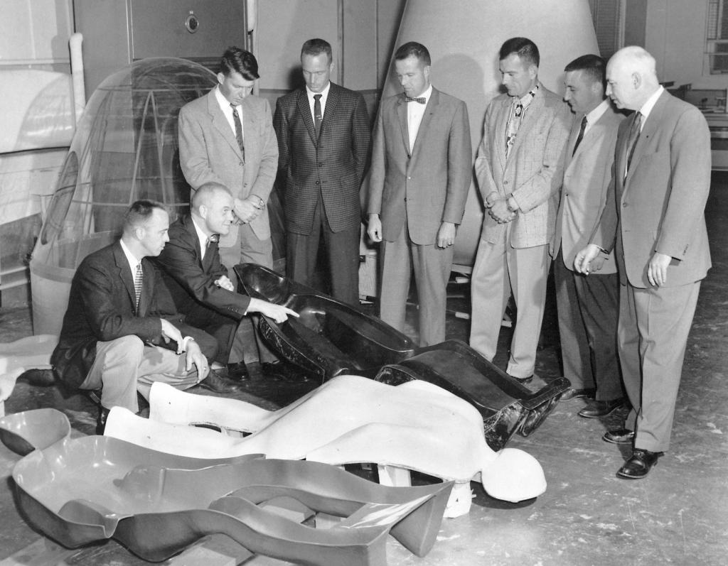 The Mercury 7 astronauts and Bob Gilruth examine an astronaut couch, which was molded to fit each of their bodies to protect them from the G-loads of launch.