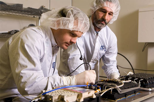 Two men in white lab coats work on a piece of equipment