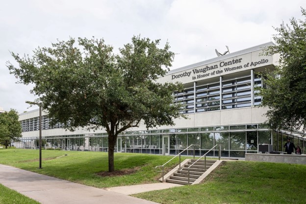 A white building stands on the Johnson Space Center campus with the words "Dorothy Vaughan Center in Honor of the Women of Apollo" on the side.