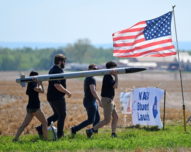 4 Students walk with their rocket on their shoulders at the Student Launch Competition  