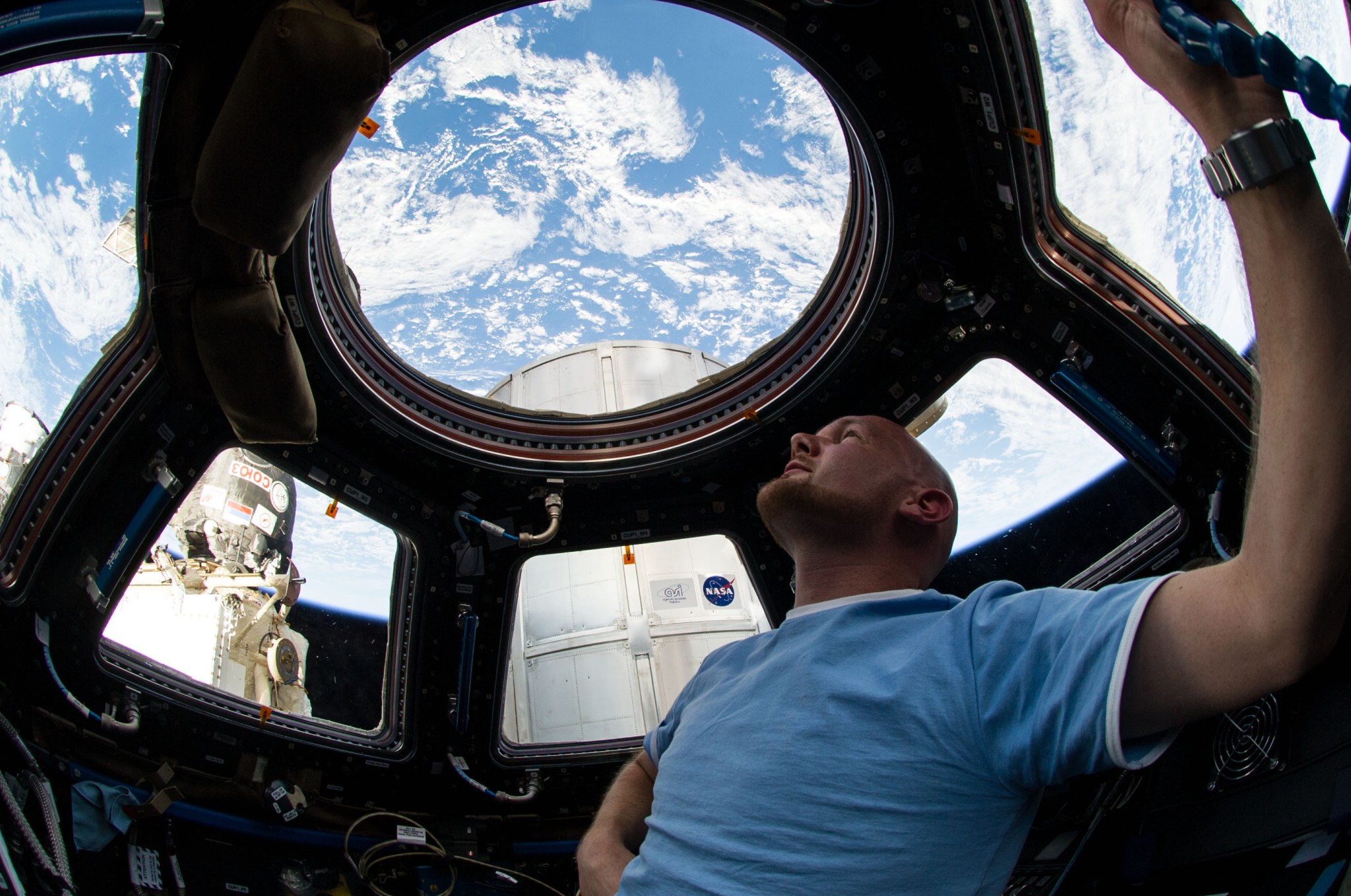 European Space Agency astronaut Alexander Gerst, Expedition 40 flight engineer, enjoys the view of Earth from the windows in the Cupola of the International Space Station. A blue and white part of Earth is visible through the windows.