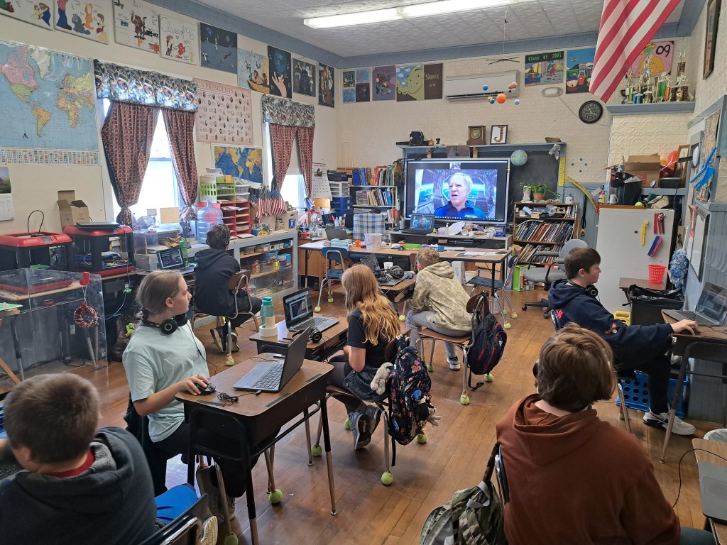 Photo of children in a classroom with an astronaut on a television screen