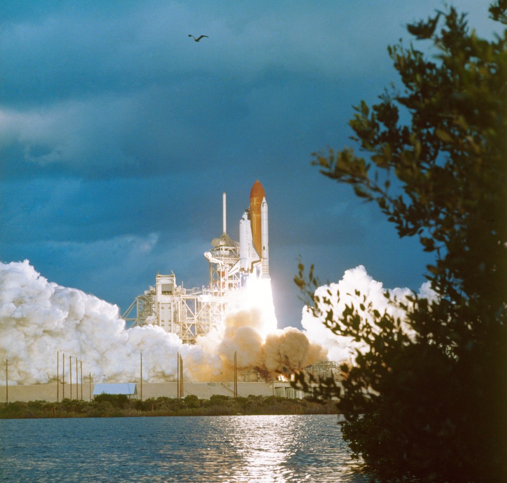 View across the water of the launch of STS 51-A shuttle Discovery. The orbiter is just clearing the launch pad