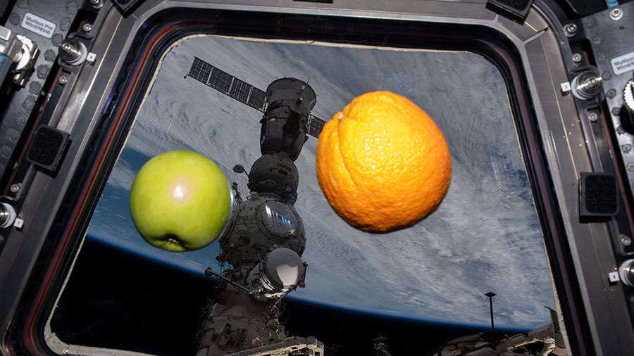 An apple and an orange float weightlessly inside the cupola with the Soyuz MS-23 crew ship docked to the Prichal docking module outside.