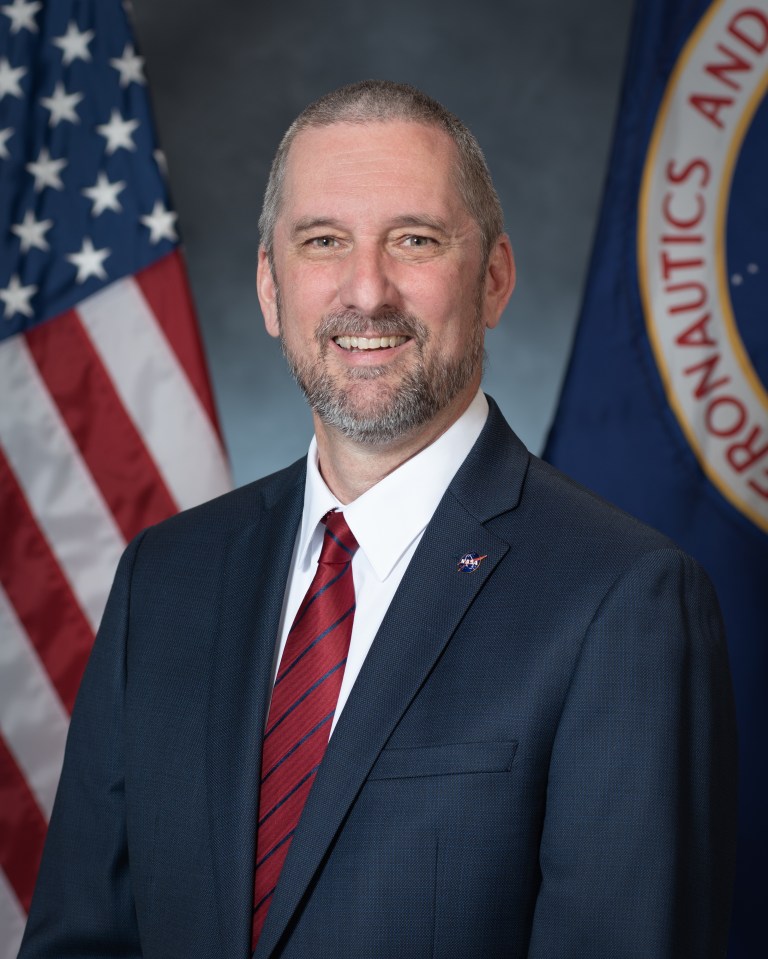 John L. Evans sits in front of American Flag to pose for photo.