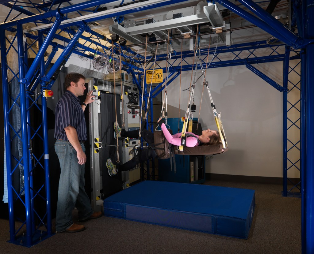Spotter Brent Crowell monitors Test Subject Liz Goetchius as she works out on the Vertical Treadmill (sZLS) in the NASA Flight Analog Research Unit (FARU) at University of Texas Medical Branch in Galveston, Texas. Photo Date: December 14, 2011. Location: UTMB - Galveston.