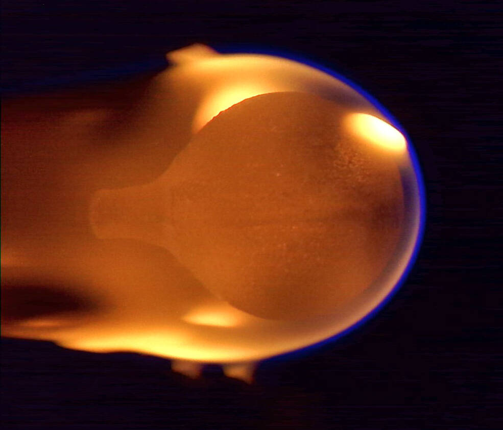 Esta imagen muestra una esfera de acrílico de 4 cm de diámetro quemándose en microgravedad. La llama naranja aparece cerca del final de la combustión, después de haber engullido toda la burbuja de combustible y de que el pequeño punto de ignición en el lado derecho se hiciera más grande.